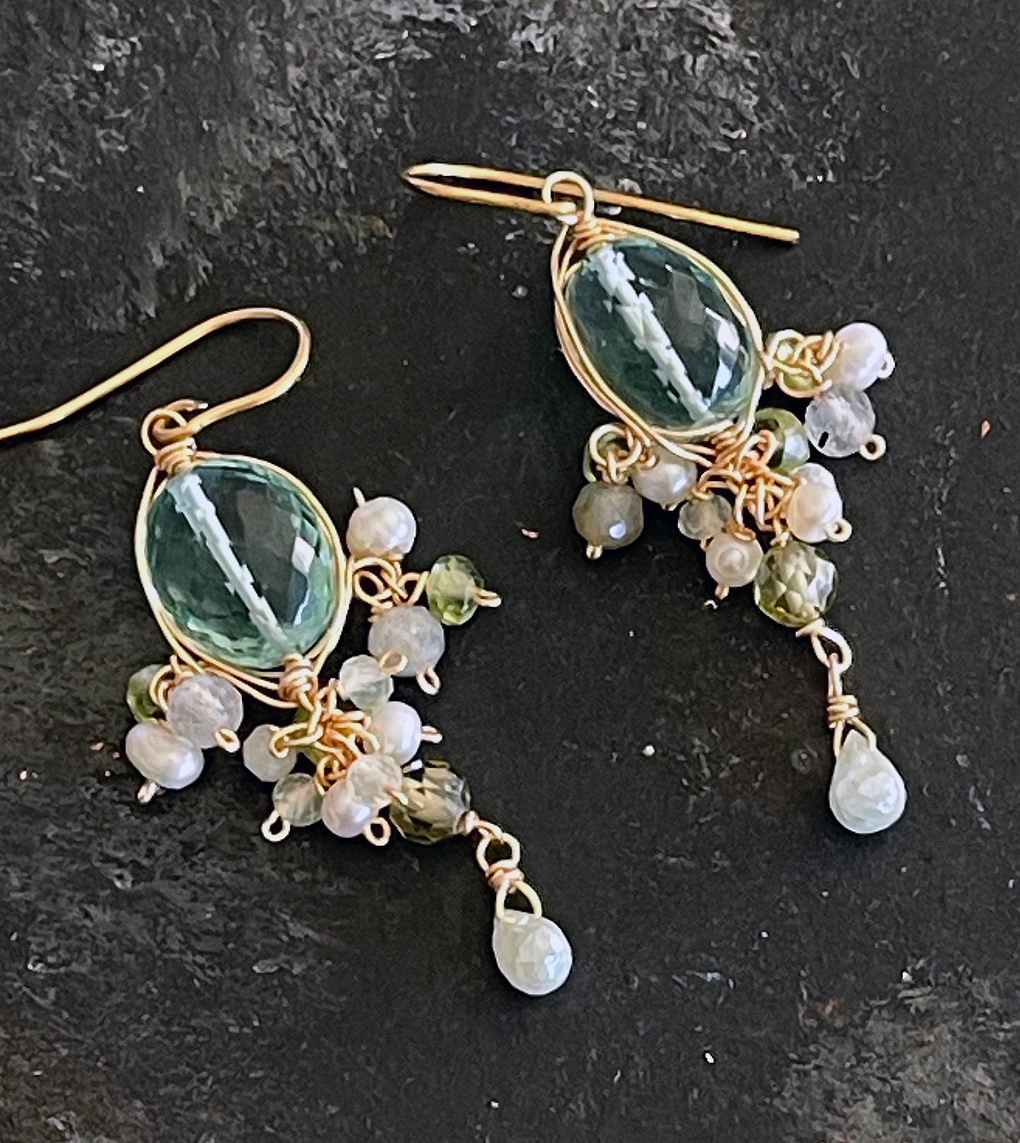 Pair of gold wire wrapped
earrings with sea green quartz and tiny pearls and gemstones on a dark surface