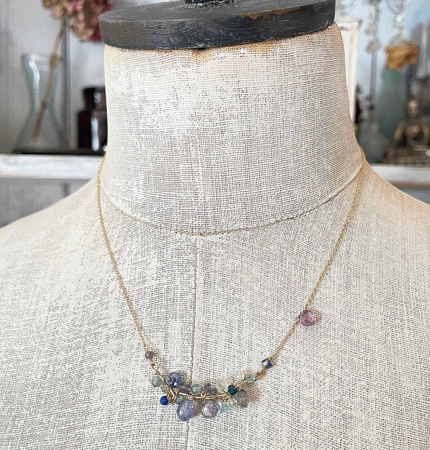 A delicate blue gemstone cluster necklace displayed on a vintage mannequin torso, showcasing its elegant drape and layered blue hues.