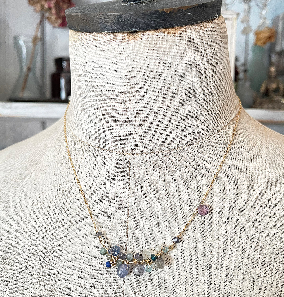 A delicate blue gemstone cluster necklace displayed on a vintage mannequin torso, showcasing its elegant drape and layered blue hues.