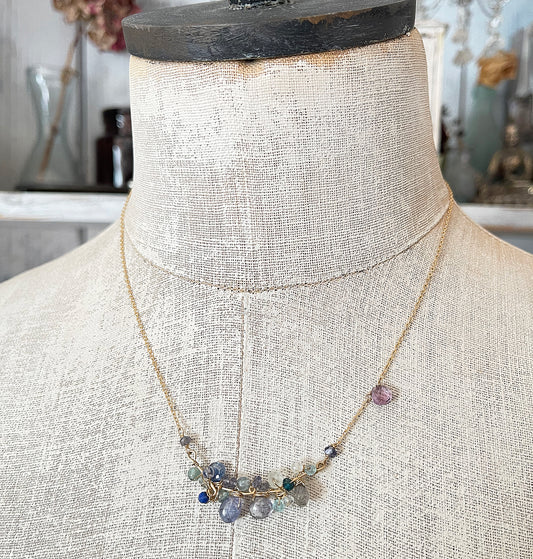 A delicate blue gemstone cluster necklace displayed on a vintage mannequin torso, showcasing its elegant drape and layered blue hues.