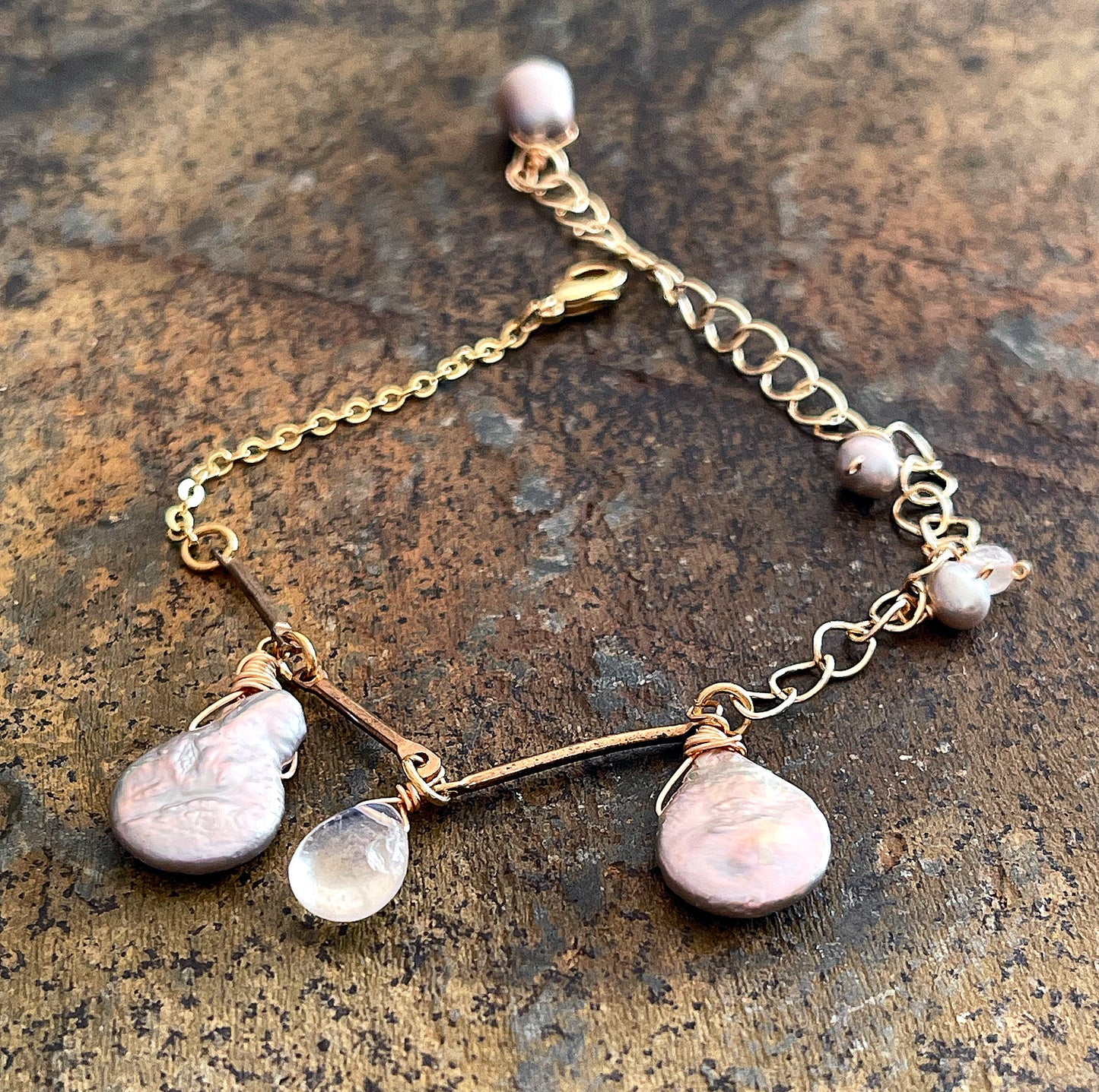 Close-up of a gray Keshi pearl and moonstone bracelet, showing the detailed gold wire wrapping and the shimmering luster of the organic pearls.