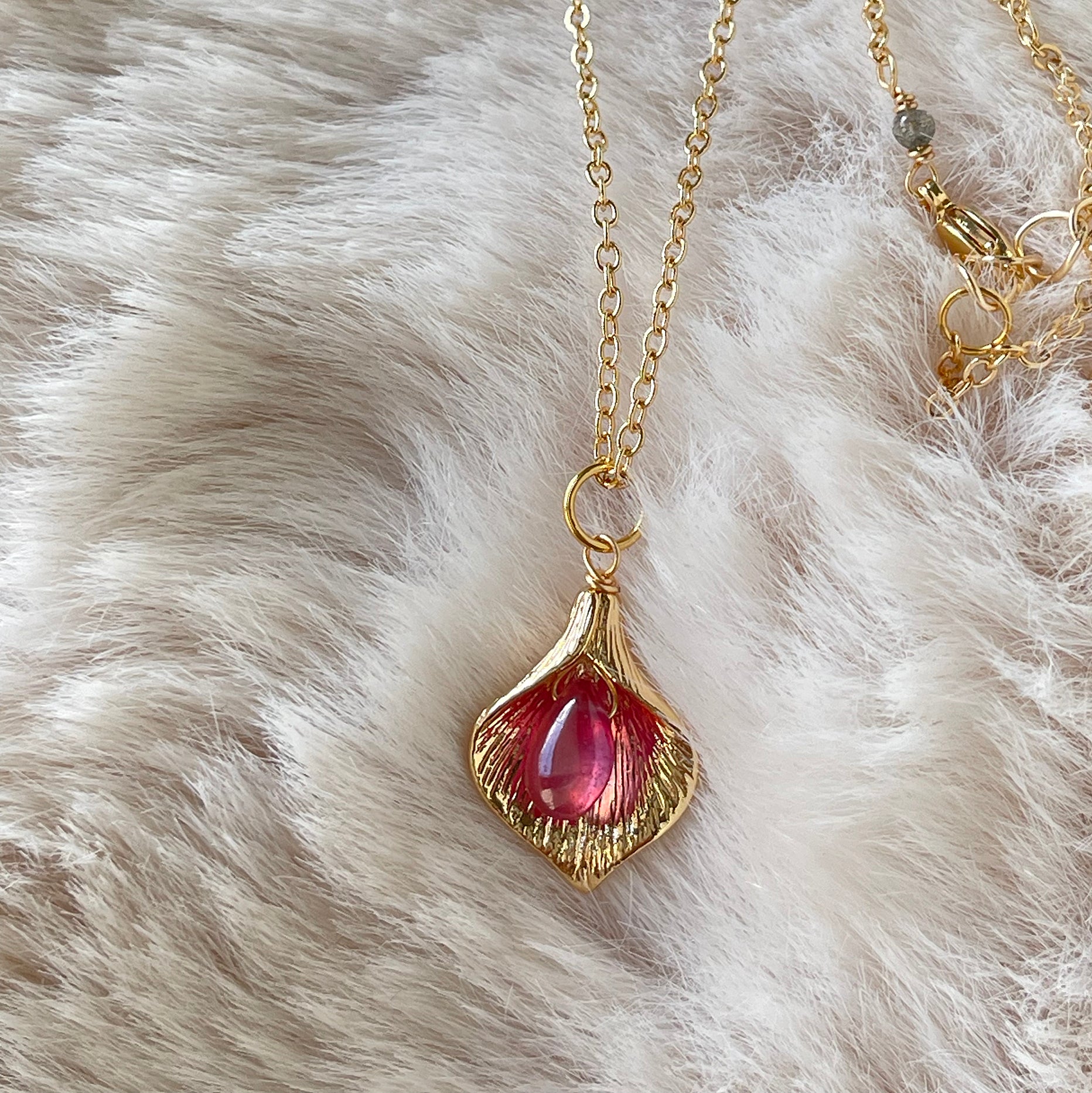 Close-up of a LuLu Jewel Design necklace featuring a teardrop ruby set inside a gold Calla Lily leaf charm on a soft faux fur background.