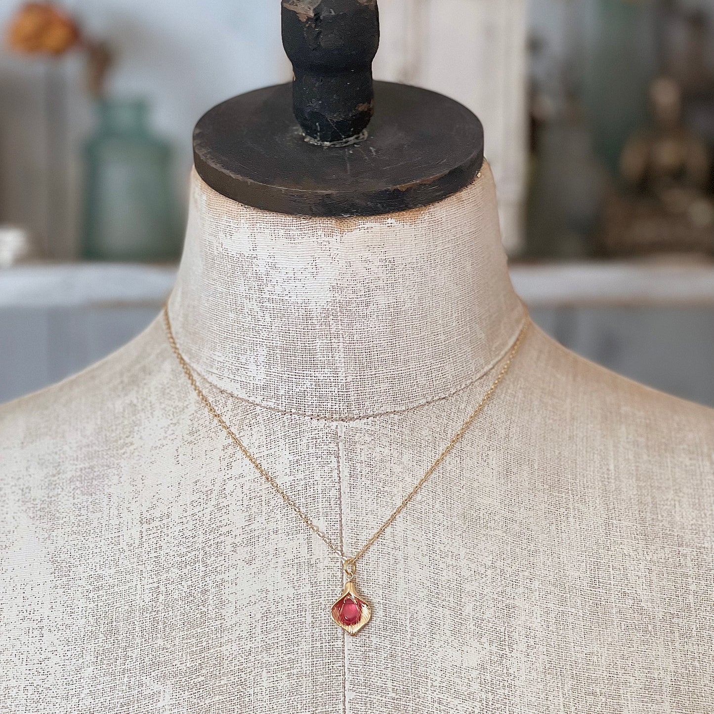 A gold Calla Lily ruby necklace displayed on a vintage-style mannequin torso, showing the elegant length and fit.