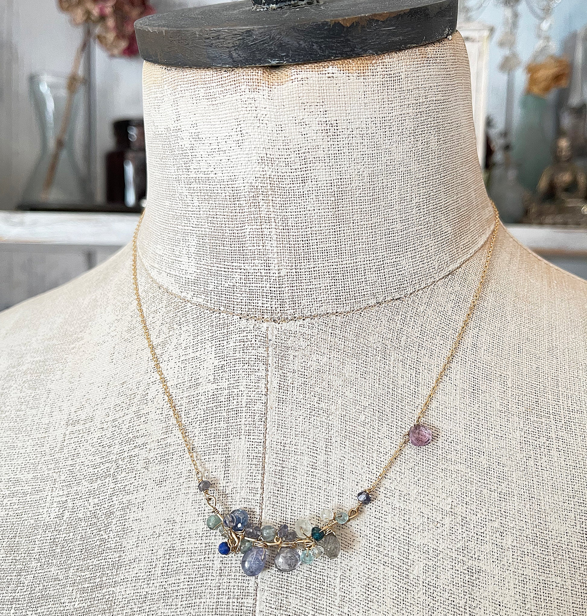 A delicate blue gemstone cluster necklace displayed on a vintage mannequin torso, showcasing its elegant drape and layered blue hues.