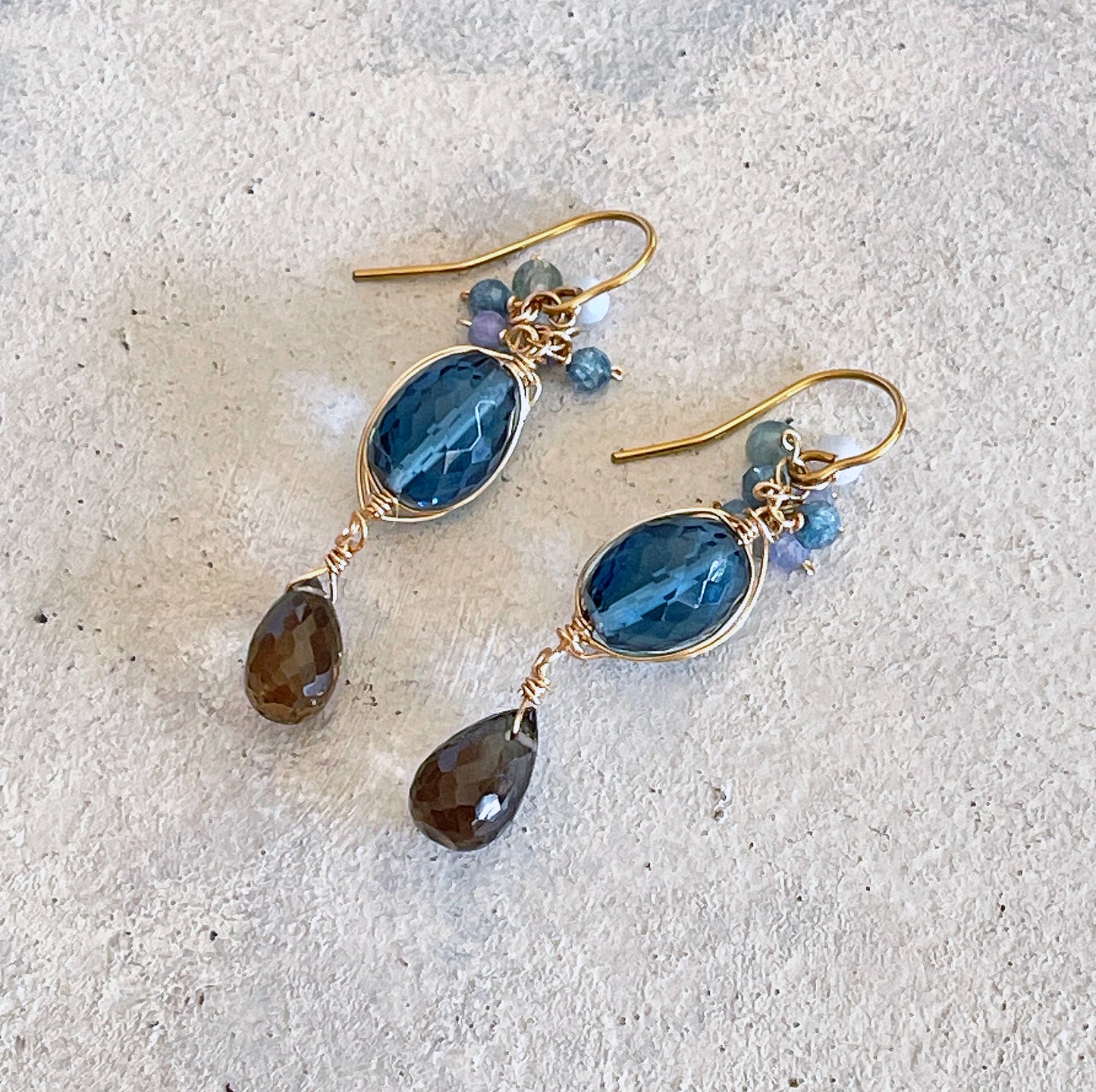 pair of deep blue quartz with smoky quartz wire wrapped dangle earrings on white textured surface